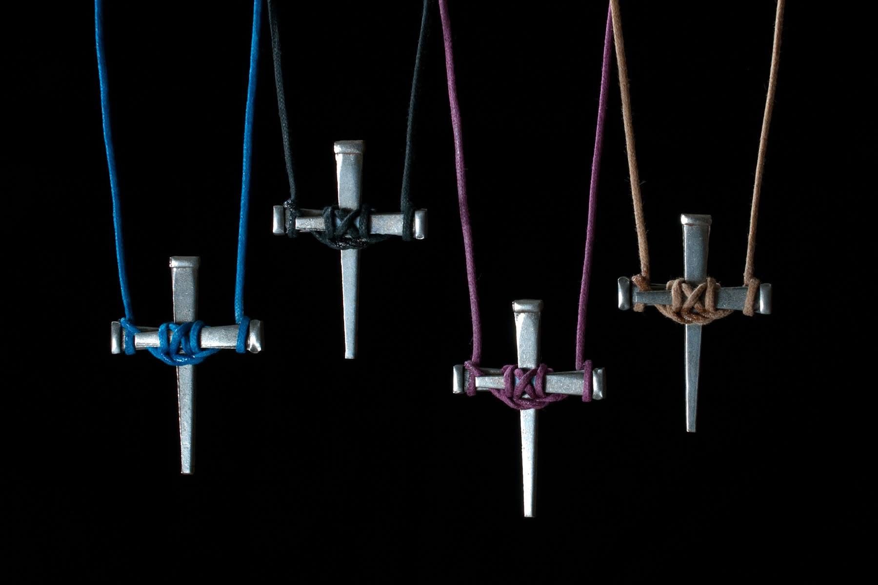 Four handmade nail crosses hanging from blue, black, burgundy, and tan cords