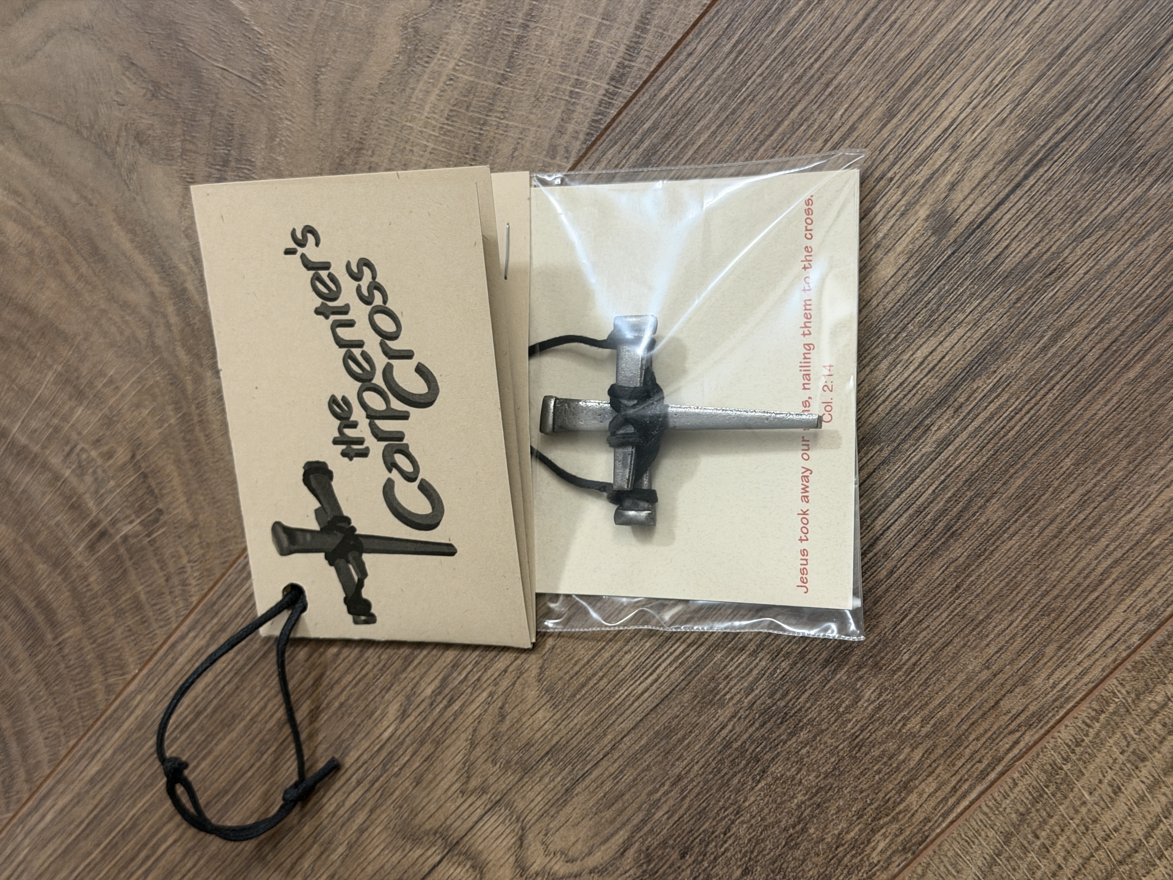 A finished Carpenter’s Cross in its clear bag with its printed message card on a wooden tabletop